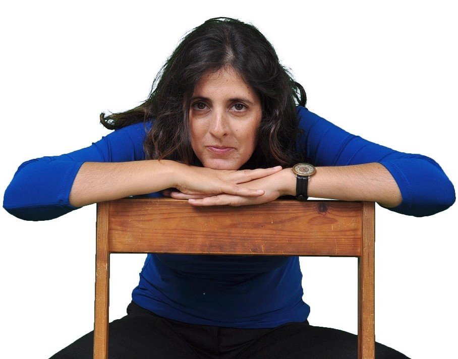 woman-in-blue-shirt-nrown-hair-sits-on-a-chair-her-hands-on-the-backrest